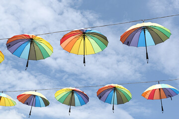 Colorful umbrella hanging on a wire against a bright blue sky