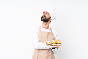 Young man holding muffin cake over isolated white background looking up while smiling
