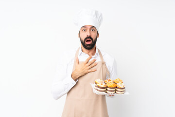 Young man holding muffin cake over isolated white background surprised and shocked while looking...