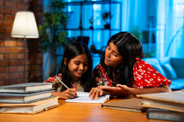 Elder Indian girl helping younger sister with homework at study table in home environment