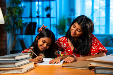 Elder Indian girl helping younger sister with homework at study table in home environment