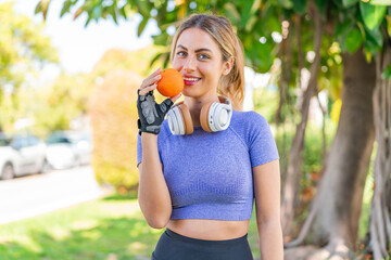 Young pretty sport woman at outdoors holding an orange