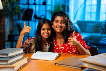 Elder Indian girl helping younger sister with homework at study table in home environment