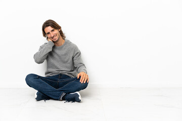 Young handsome man sitting on the floor over isolated background laughing