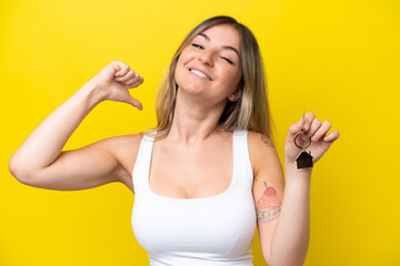 Young Rumanian woman holding home keys isolated on yellow background proud and self-satisfied