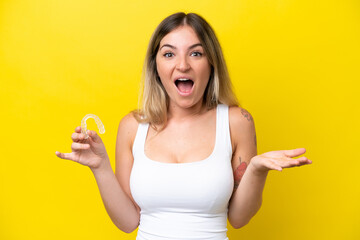 Young Rumanian woman holding envisaging isolated on yellow background with shocked facial expression