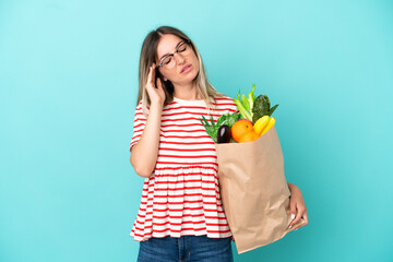 Young woman holding a grocery shopping bag isolated on blue background with headache