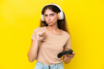 Young caucasian woman playing with a video game controller isolated on yellow background proud and...