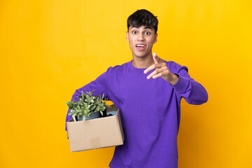 Man making a move while picking up a box full of things surprised and pointing front