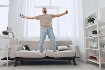 Energetic man celebrating at home, expressing joy with outstretched arms. Bright, modern living...