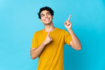 Young Venezuelan man isolated on blue background pointing with the index finger a great idea