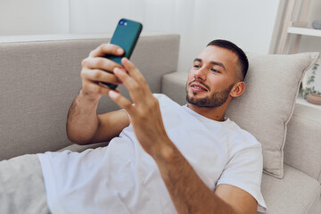 Relaxed man using smartphone on a comfortable couch, engaging with technology in a modern living...