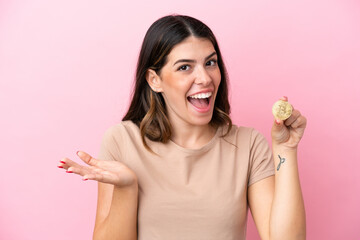Young Italian woman holding a Bitcoin isolated on pink background with shocked facial expression