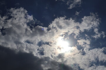 Bright sun shining through white clouds in blue sky
