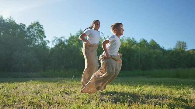Boy leads sack race game. Girl and boy jumping outdoors in summer field. Kid enjoys summer competition. Girl tries to catch boy. Game for children. Jumping kids outdoors play competition together.