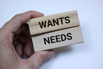Hands holding wooden blocks with text 'wants' and 'needs' symbolizing decision making and priorities isolated on white background