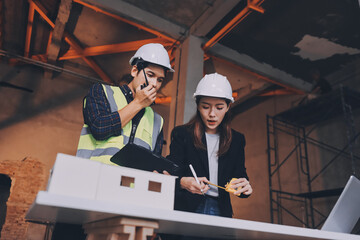 Construction manager and engineer dressed in orange work vests and hard helmets explore...
