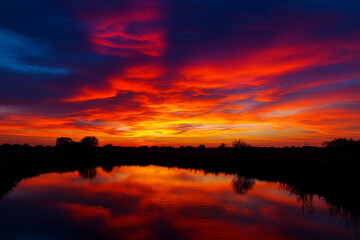 Vibrant fiery sunset over a calm lake reflecting the dramatic crimson and orange sky