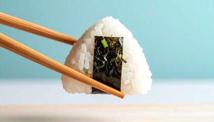 Japanese onigiri rice ball with seaweed filling held by chopsticks, closeup shot