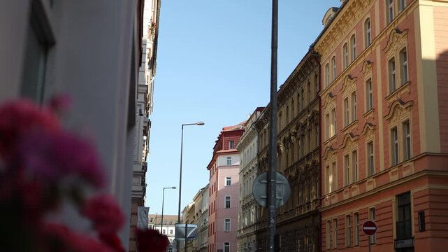 Colorful historic buildings rise along a narrow European street under bright blue sky with decorative facades and soft sunlight creating a warm urban scene full of architectural charm