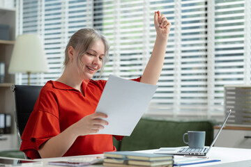 Smiling young woman succeeding in business using laptop and computer while doing some paperwork at...