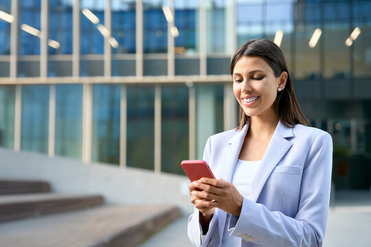 Indian middle eastern female entrepreneur businesswoman holding mobile cell phone for work outdoors. Young latin hispanic business woman using smartphone cellphone financial trading app. Copy space
