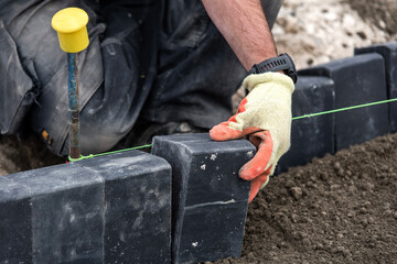 Close-up of builder laying black paving bricks on  building site