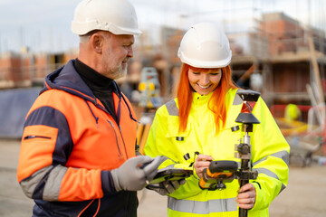 Male and female builders collaborate on-site, discussing project details while surveying at building site