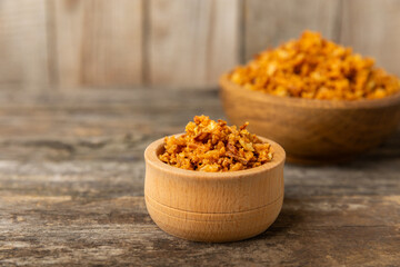 Crispy fried onions in a bowl on a wooden table. Roasted Onions. Seasoning for dishes. Spices. Salad dressing. Space for text. Copy space