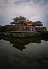 Obraz premium Majestic entrance of Hue Imperial City reflected in tranquil waters under a dramatic cloudy sky.