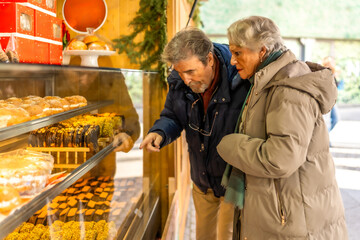 Senior couple choosing pastries at christmas market display