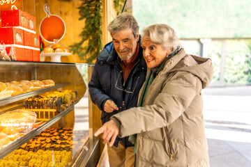 Senior couple choosing pastries at christmas market display