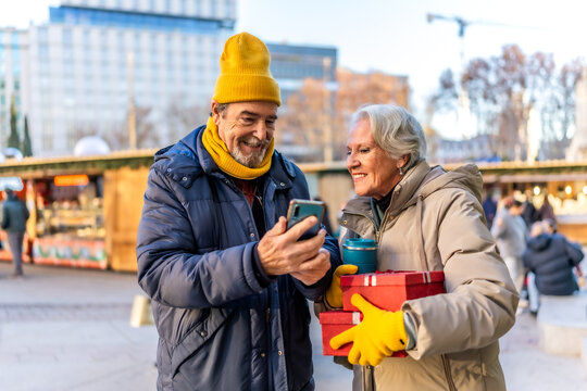 Smiling senior couple using smartphone at christmas market in winter city