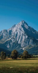 Majestic mountain peak rising over a vibrant green field and trees, under a clear blue sky