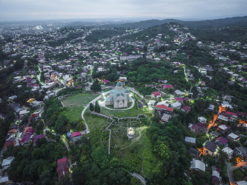 Aerial view of Bagrati Cathedral gleaming majestically atop Ukimerioni Hill amid a tapestry of terracotta roofs and verdant foliage, Kutaisi, Imereti, Georgia.