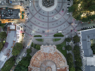 Aerial view of a circular plaza with concentric patterns and a fountain, framed by illuminated buildings and lush trees, Kutaisi, Imereti, Georgia.