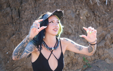 Sexy young tattooed woman with piercings and colorful hair frames a scene with her hands under...