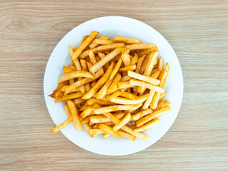 Crispy golden french fries on white plate on wooden surface