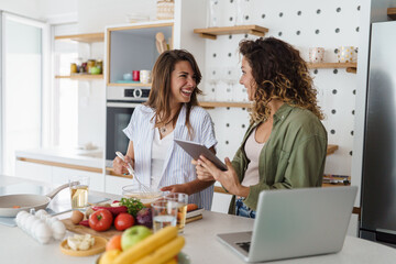 Young Women Cooking in Modern Well-Lit Kitchen with Fresh Ingredients and Smiling Expressions