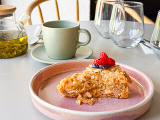 Slice of layered cake with berries served with tea in cafe. Dessert and beverage symbolizing sweet indulgence, lifestyle dining and culinary culture.