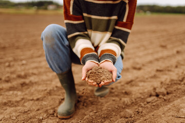 Close up of agronomist holding black soil and pouring it on agricultural field. Young female farmer checking soil quality by touching it with her hands. Agriculture concept. Farming.