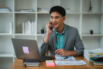 Fototapeta premium Asian businessman talking on phone and working with laptop in office
