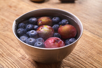 Fresh Ripe Plums and Blueberries in a Bowl on a Wooden Table