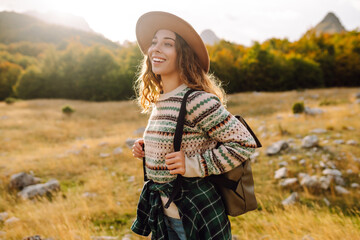 Portrait of a young woman with a backpack and a hat walking along a path in the mountains. The...