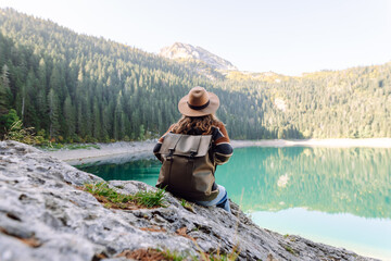 Female hiker with backpack explores mountainous area near a lake on sunny day. Young female...