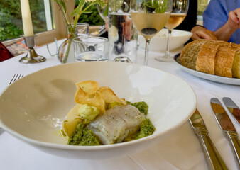 A neatly plated dish on a white plate, served on a table with white linen in a fine dining restaurant. The menu features refined dishes with colorful garnishes, carefully presented.