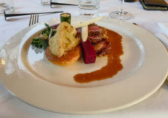 A neatly plated dish on a white plate, served on a table with white linen in a fine dining restaurant. The menu features refined dishes with colorful garnishes, carefully presented.