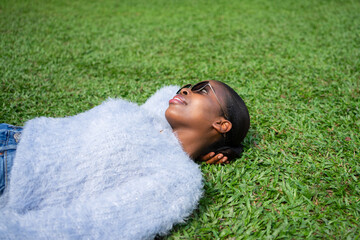Young black woman relaxing lying on grass wearing sunglasses and dreaming
