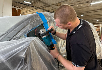 A man polishes the glass of a car with a polishing machine from small scratches with a large one....