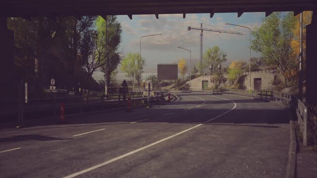 A construction site is visible in the background as vehicles approach a winding roadway. Lush trees line the sides, under a blue sky with scattered clouds.